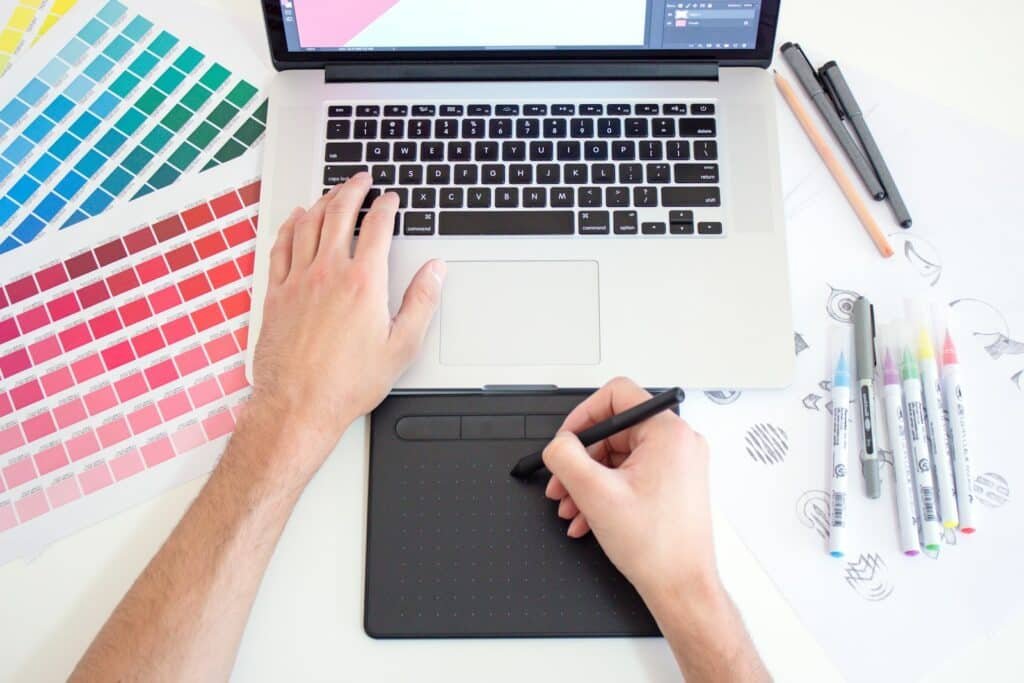 Graphiste travaillant sur ordinateur avec tablette graphique et nuancier de couleurs